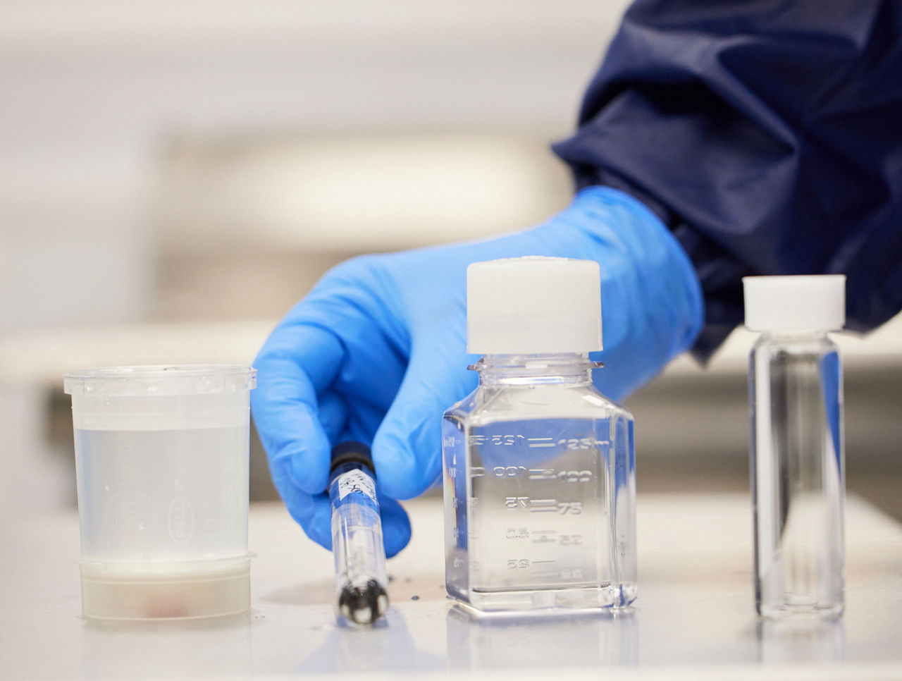  Close up of gloved hand preparing various water samples for testing